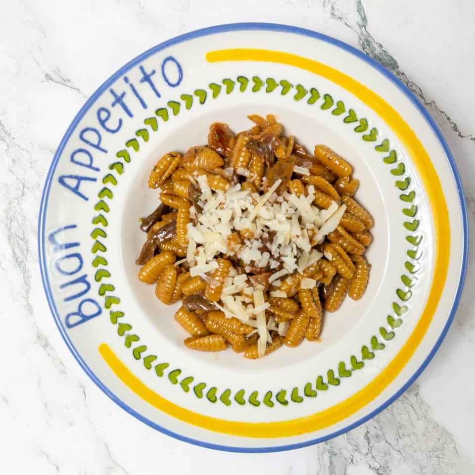 Ridged pasta with mushrooms and grated cheese served on a colorful decorative plate atop a marble surface.