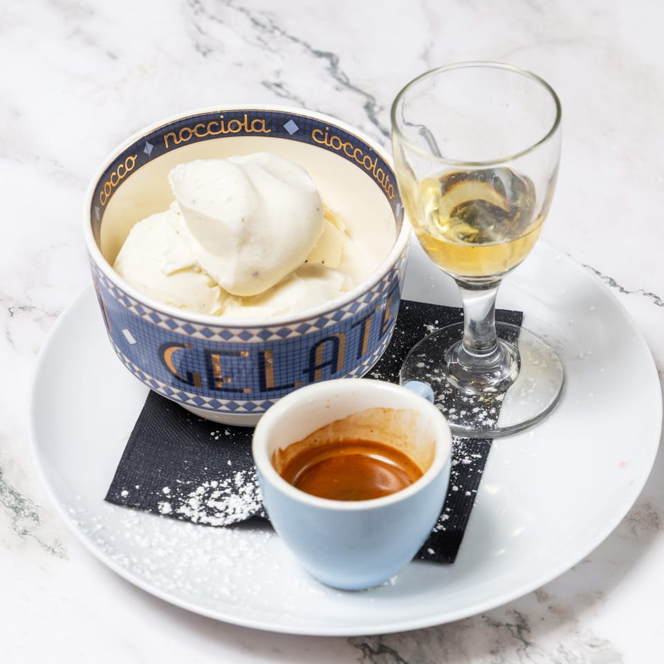 Scoop of vanilla gelato, espresso, and a glass of golden liqueur arranged on a white plate atop marble.