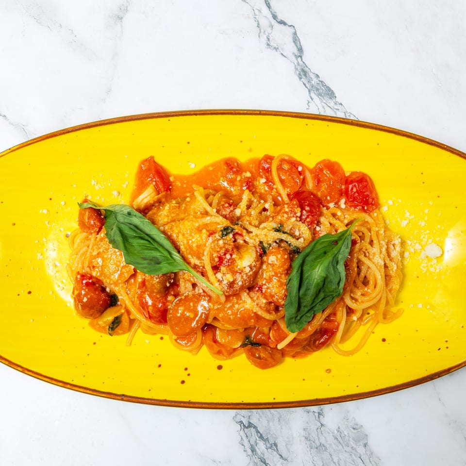 Spaghetti with tomato sauce, cherry tomatoes, basil leaves, and grated cheese served on a bright yellow platter.