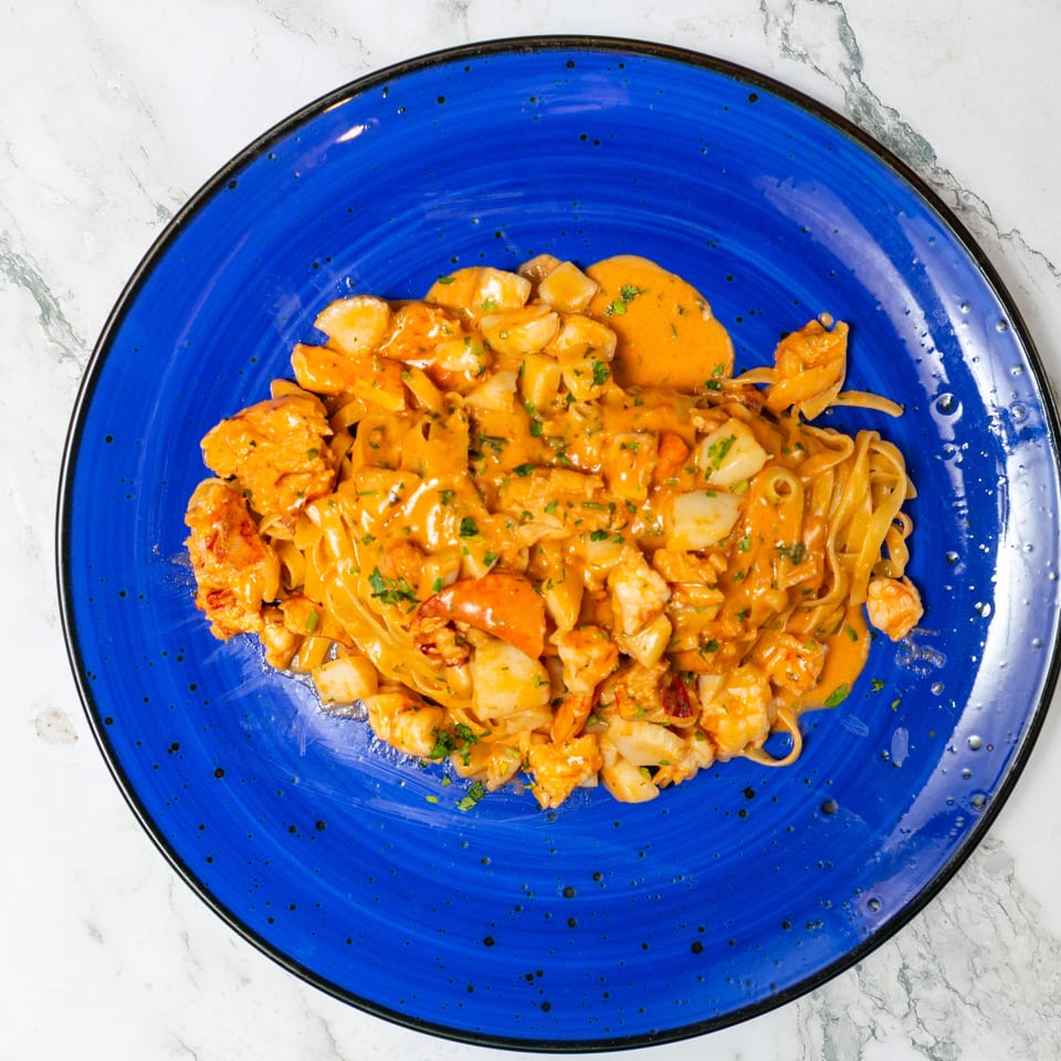 Creamy seafood pasta with shrimp, lobster, scallops, and herbs served on a blue plate.