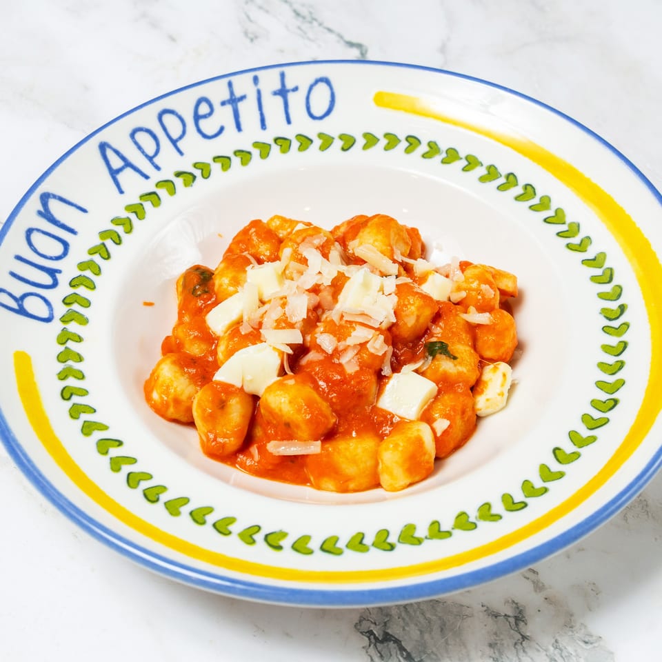 Gnocchi in tomato sauce topped with mozzarella and grated cheese, served on a colorful ceramic plate.