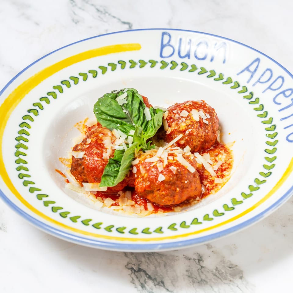 Italian meatballs in tomato sauce topped with grated Parmesan and fresh basil, served on a decorative plate.